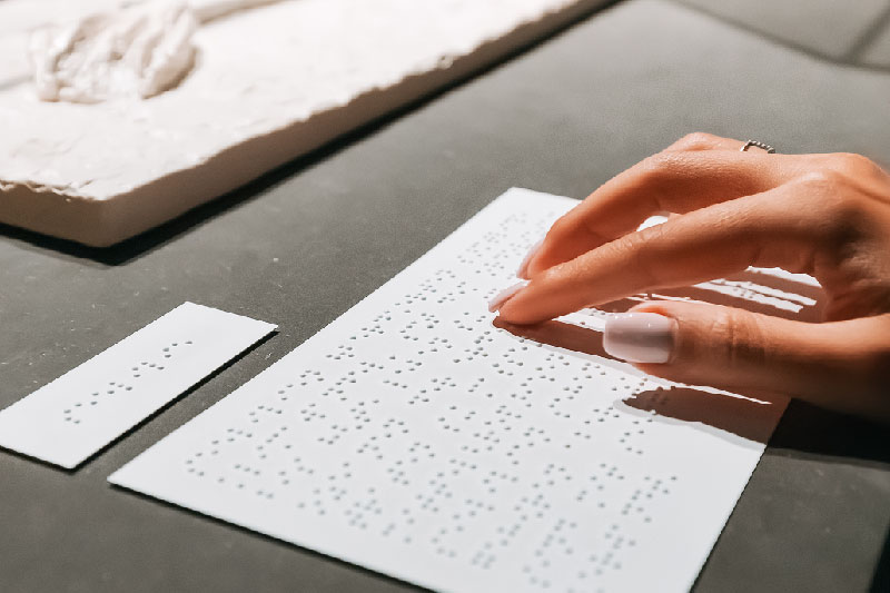 Dłoń dotykająca tekstu w alfabecie Braille'a