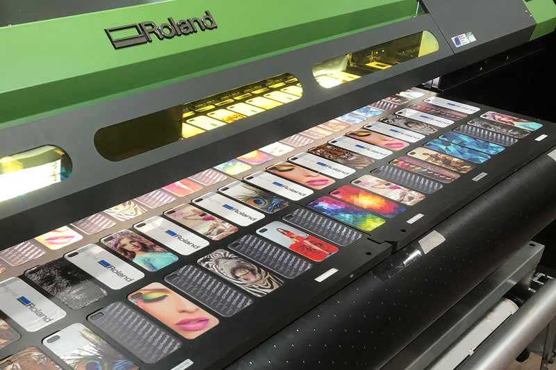 Roland UV-Drucker der S-Serie mit einem Druckbett, das mit bedruckten Handyhüllen in verschiedenen Designs voll bestückt ist 