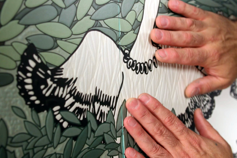 Hands installing custom printed wall graphics featuring a black-and-white animal illustration and leafy pattern.