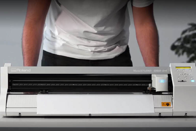 A person loading a vinyl cutter with white vinyl