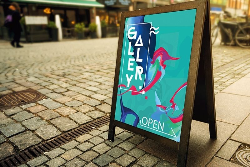 Une affiche annonçant l'ouverture d'une galerie, sur un support chevalet posé sur le trottoir