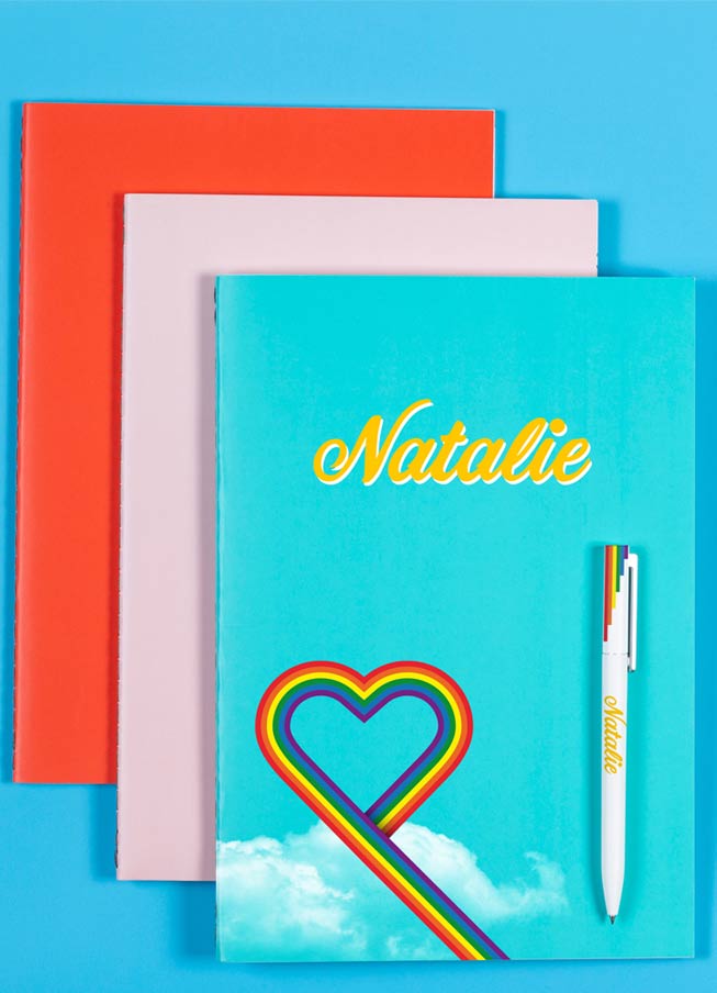 Three notebooks in red, pink and blue with rainbow heart and name printed on the front and personalised pen accessory